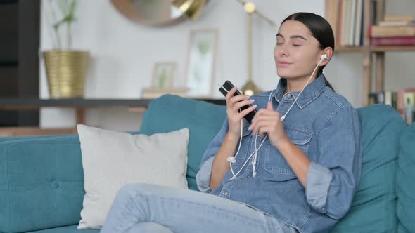 Latin Woman Listening To Music on Smartphone on Sofa