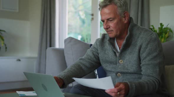 Animation of caucasian senior man doing paperwork and using laptop at home