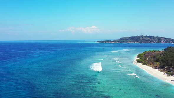 Peaceful exotic beach with white sand washed by ocean waves foaming over calm clear water of turquoi