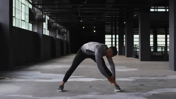 African american man stretching his legs in an empty urban building