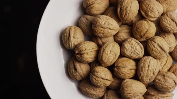 Cinematic, rotating shot of walnuts in their shells on a white surface 