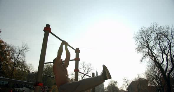 The Young Man Jumps on the Horizontal Bar and Does Pull Ups with a Narrow Grip in Good Weather 