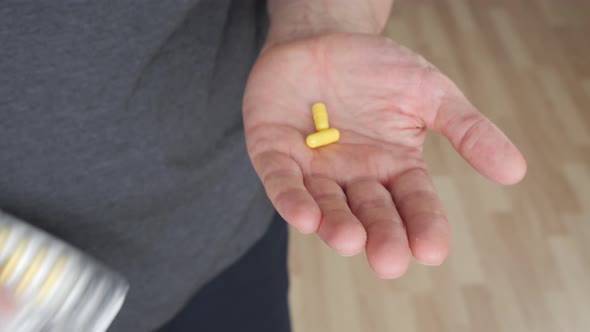 Close Up View of Male Hand Holding Yellow Capsules