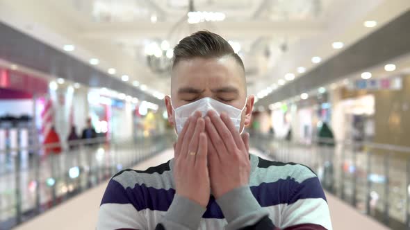 A Young Man in a Medical Mask in a Shopping Center. The Man Is Coughing. The Masked Man Protects