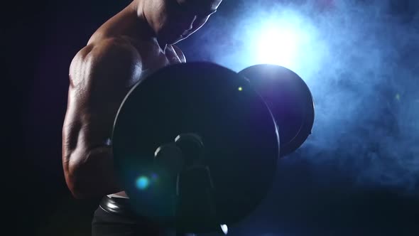 Bodybuilder Lifts a Bar To Train for Competitions. Black Smoke Background. Slow Motion