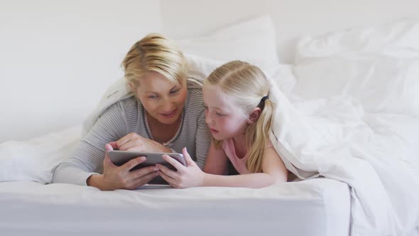 Front view of Caucasian woman and her daughter using digital tablet on bed