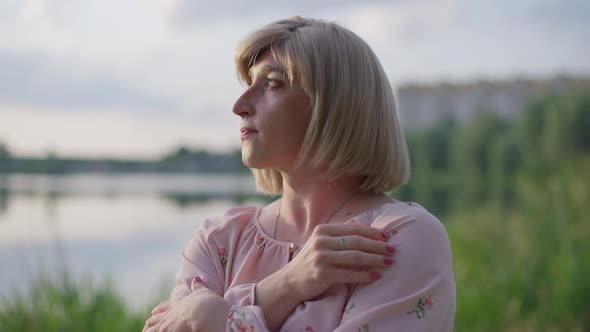 Thoughtful Adult Caucasian Trans Woman Admiring Sunset on Lake Looking Away