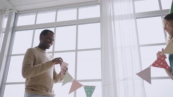 Multinational Couple Hangs Colorful Pennant Banners in Room