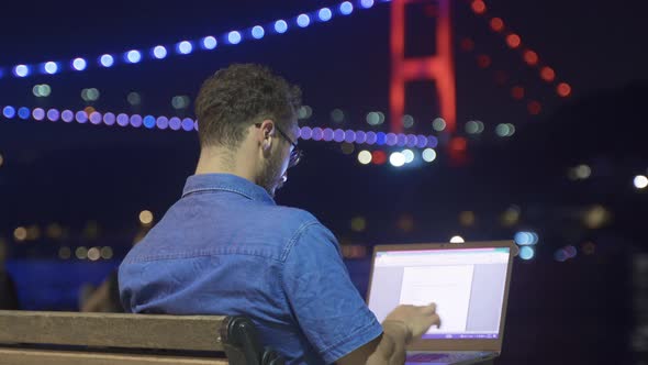 Man doing work on laptop against night sea view.