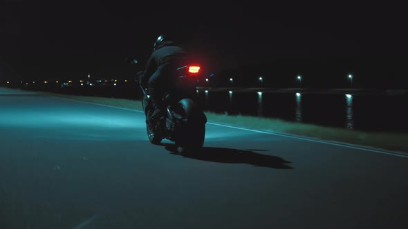 A Man Rides a Sports Motorcycle Through the City at Night Against the Backdrop of the River
