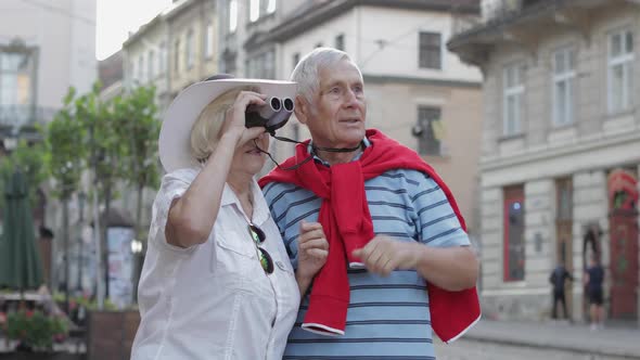 Senior Male and Female Tourists Walking in Town Center and Looking in Binoculars