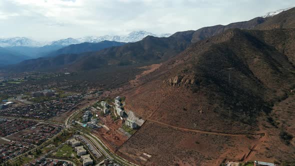 Aerial orbit of Morro Las Papas and a residential neighborhood in the foothills, snowcapped El Plomo