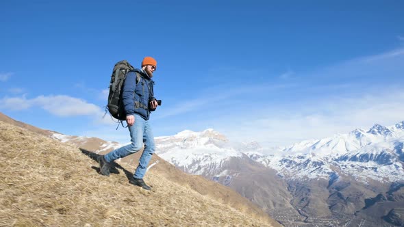 Bearded Young Male Photographer in a Hat and Sunglasses with a Large Backpack and a Camera Around