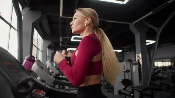 Beautiful Athletic Woman is Jogging in Gym on Treadmill Side View