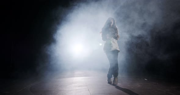 Young female dancer performing wild hip hop dance with light and smoke background