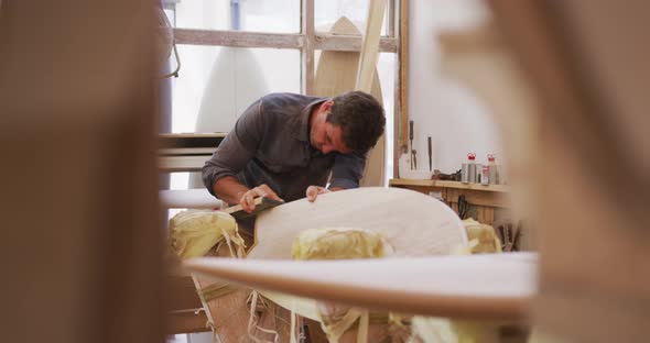 Caucasian male surfboard maker working in his studio and making a wooden surfboard