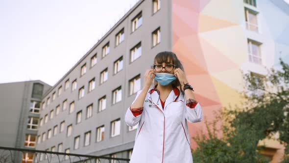 Young Female Intern or Medical Student Taking Off Surgical Face Mask and Looking at Camera