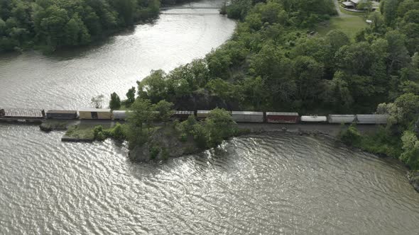 Drone shot of a long cargo train going into a tunnel, flying down and panning to the left.