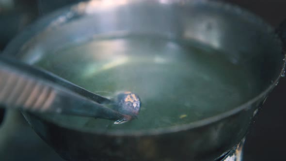 Jeweler Puts Metal Drop Into Cup with Liquid in Shop Closeup