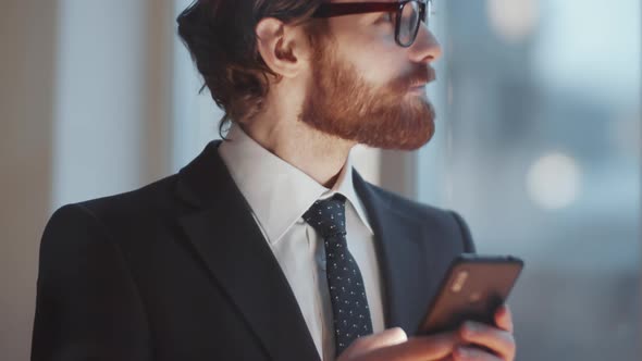 View through Glass Wall of Businessman Using Smartphone in Office