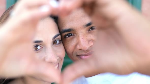 Closeup portrait of happy young multiethnic couple smiling and doing heart sigh with their hands