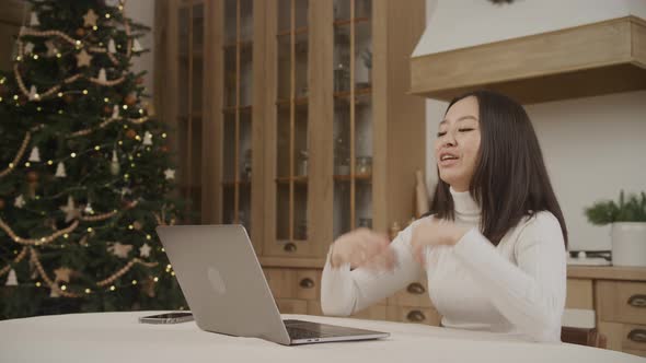 Young Adult Asian Woman on a Video Call on Her Laptop with a Christmass Tree on Background Indoors