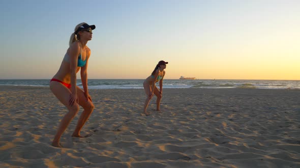 Women teams play beach volleyball at sunset and a player passes the ball.