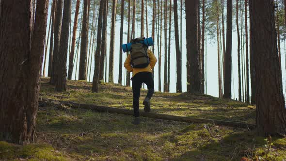 African Black Man Climbs Uphill in Woods in Yellow Jacket with Backpack in Slow Motion