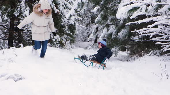 A Mother Sleds Her Son in a Snowcovered Forest at a Ski Resort in Winter