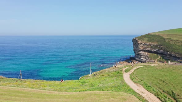 Tourists walking in border of green blue turquoise seaside cliff. Aerial