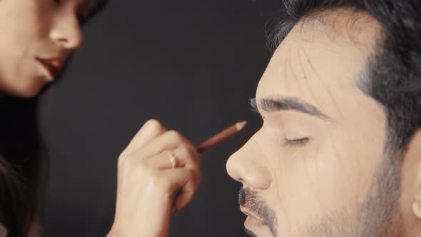 Make up artist drawing the lines on man's face to prepare for prosthetic insert for Halloween mask
