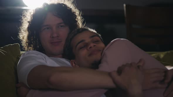 Lockdown of Young Gay Couple in Embrace on Couch in Living Room Having Rest and Watching Movie
