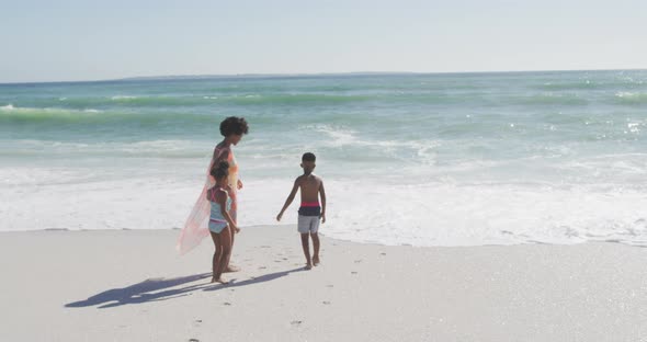 Smiling african american mother with children wearing swimming suits on sunny beach