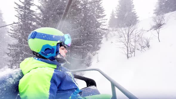 Boy Skier in Helmet and Mask on the Ski Lift During Snowfall