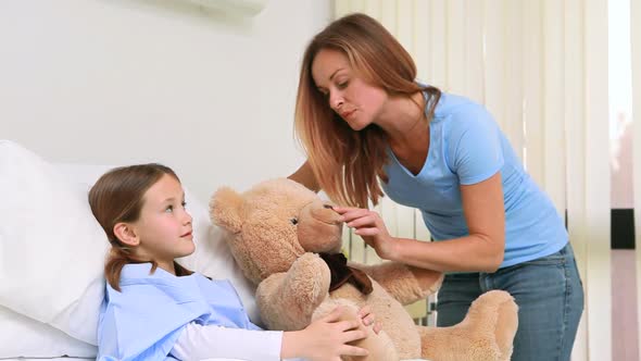 Smiling woman while giving a teddy bear to a girl in a bed