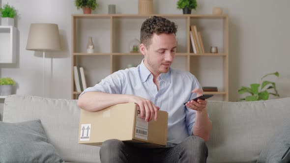 Man Holds Smartphone While Sit on Sofa with Box Using Parcel Tracking Application Leave Positive