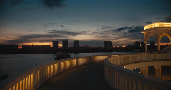 Beautiful Evening View Pier, Boat Is Sailing Along River. Sunset Over River Against Background City