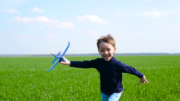 A Happy, Laughing Boy Runs Across a Green Field Against a Blue Sky, Holding a Toy Airplane in His