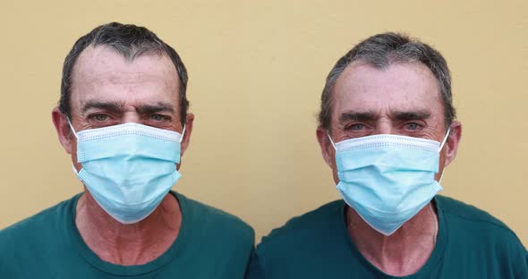 Senior twin men looking and smiling while wearing safety face masks for coronavirus outbreak