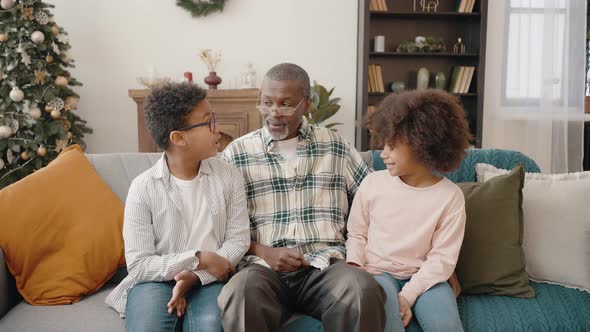 Happy Senior African American Grandfather Talking to Grandchildren Sitting at Living Room with Xmas