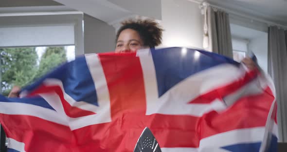 Happy African American Young Woman Shaking British Flag Smiling Cheering for Team Watching TV Match