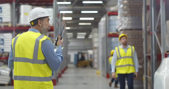 Senior Manager in Safety Uniform Transferring Message to Employee with Walkietalkie in Warehouse
