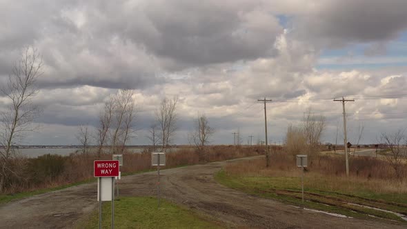 A low angle drone shot on a cloudy day, over a dirt road near a quiet bay. The drone camera slowly b