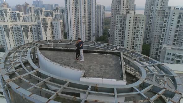 Aerial Orbital Shot of Hugging and Kissing Couple on the Roof Top of Modern Apartments Building on