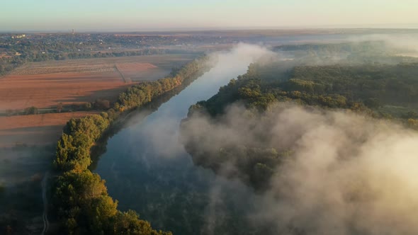 Aerial drone view of nature of Moldova at sunset. River and lush fog above it, village, greenery