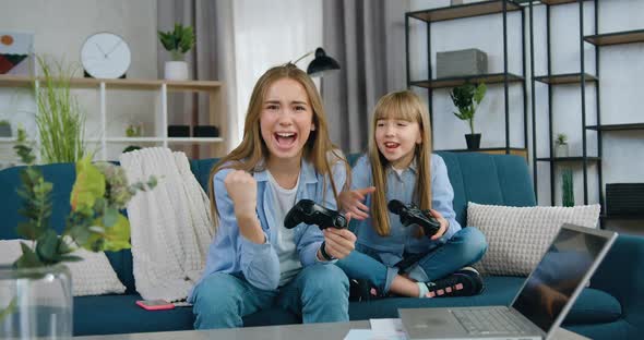 Two Different Ages Sisters Having Fun Together while Playing Video Game at Home