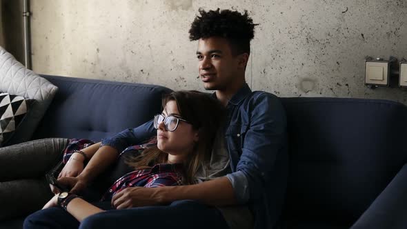 Cute Happy Couple of Young Hipsters Lying on the Couch Making Silly Facestrying to Find a Perfect Tv