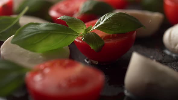 Camera follows grinding pepper over tomato and mozzarella cheese salad. Slow Motion.