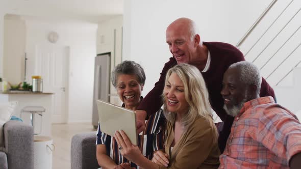 Two diverse senior couples sitting on a couch using a digital tablet and laughing