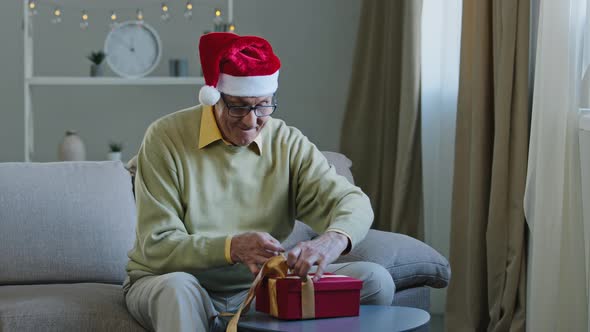 Excited Elderly Man in Santa Hat Opens Box Say Wow Show Two Thumb Up Rejoices in Unexpected Gift